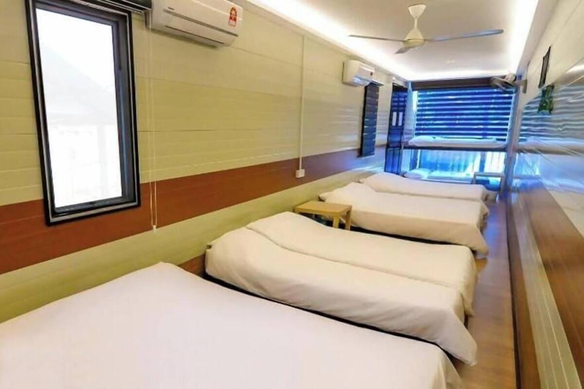 Ein Hotelzimmer mit vier nebeneinander stehenden Betten, einem Deckenventilator und einem Fenster mit Jalousien.