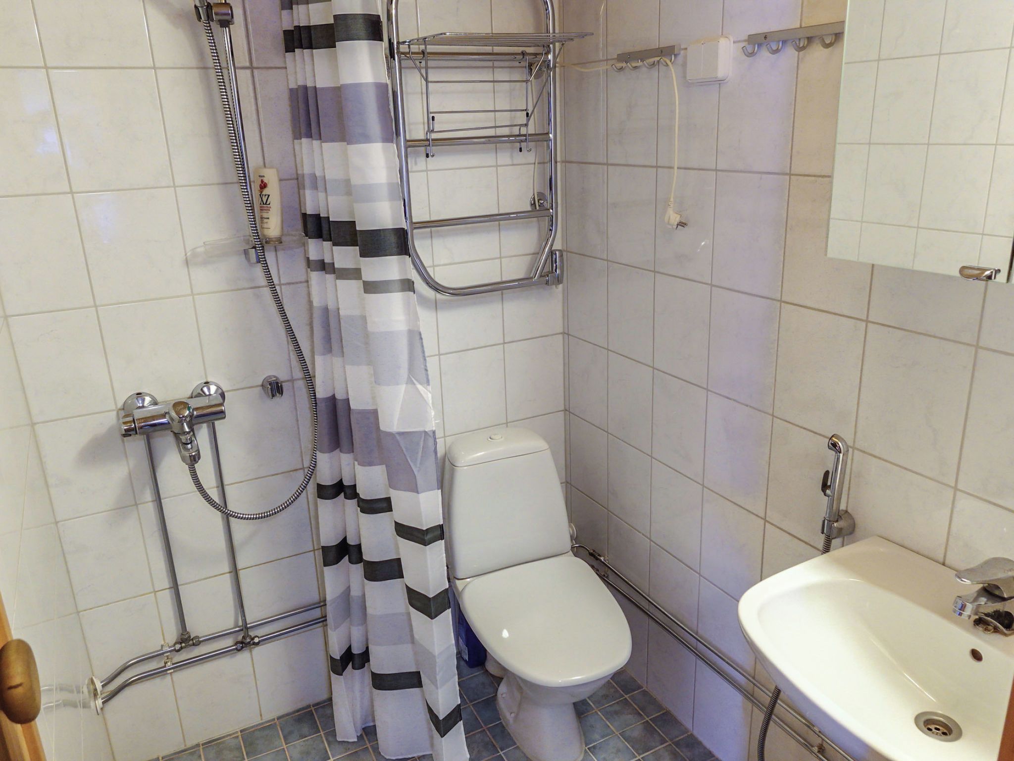 A small bathroom with a toilet, a shower with a curtain, a sink, and a towel rack.