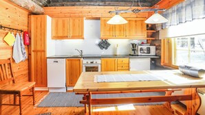 A cozy cabin-style kitchen with wooden cabinets, a dining table, and a large window. - Aihkelo by Interhome (Sodankylä)