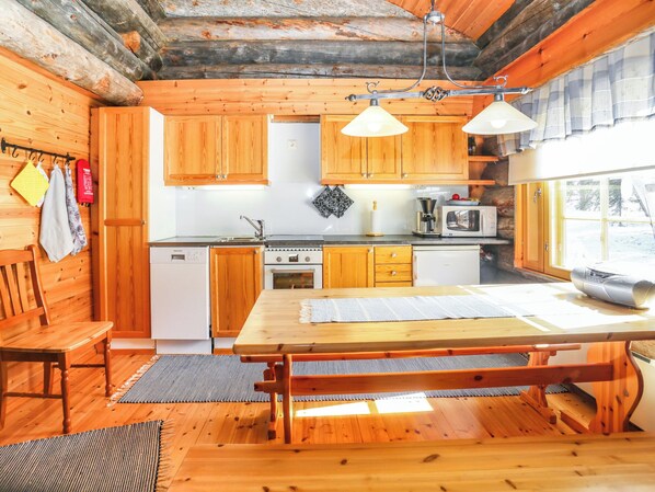 Une cuisine chaleureuse, aménagée dans le style d’un chalet, avec des meubles en bois, une table à manger et une grande fenêtre.