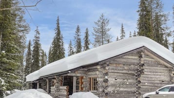 Una cabana de fusta amb un teulat cobert de neu, envoltada d'alts pins.