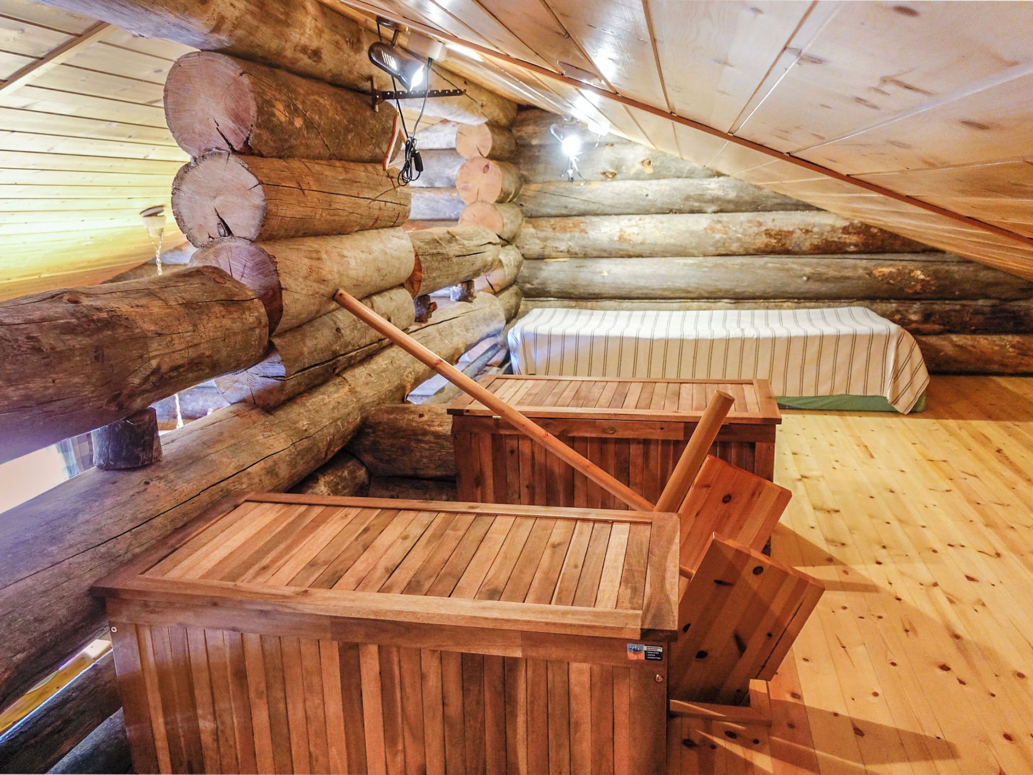A log cabin interior with a wooden bench and a bed with striped bedding.
