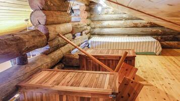 A log cabin interior with a wooden bench and a bed with striped bedding.