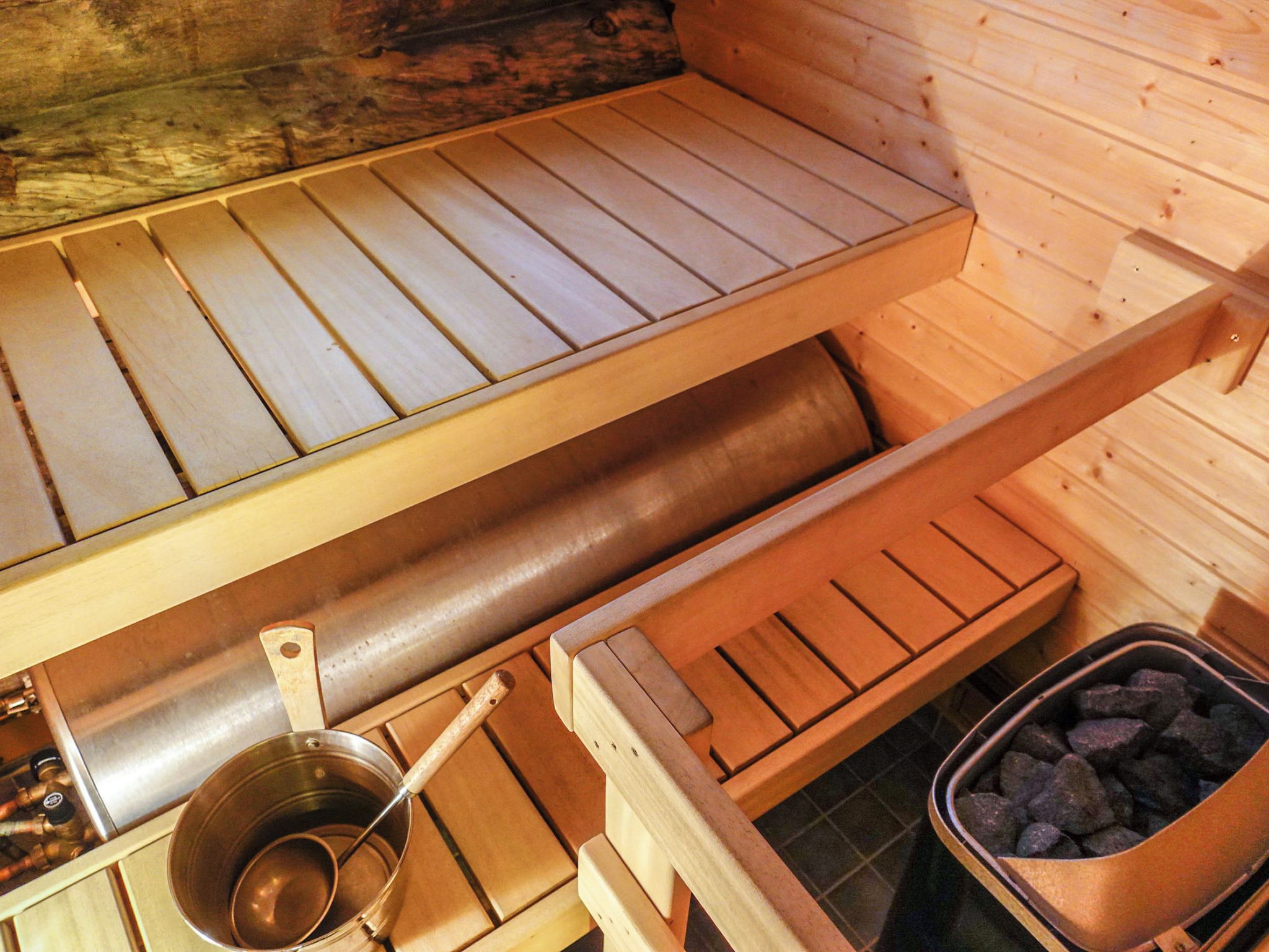 Una sauna amb bancs de fusta, una banyera metàl·lica i un recipient amb pedres.