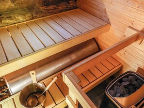 A sauna with wooden benches, a metal basin, and a container of stones. - Aihkelo by Interhome (Sodankylä)