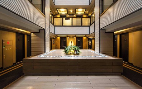 A modern hotel lobby with a central water feature, multiple elevators, and a glass-enclosed upper level.