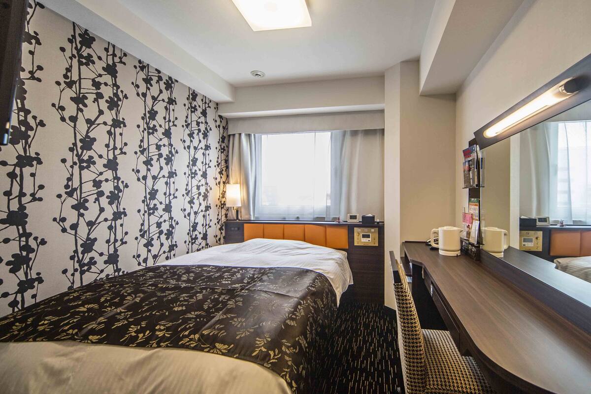 A hotel room with a bed, a desk, a mirror, and a window.