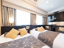 A hotel room with two beds, a TV, a desk, and a large window with curtains.