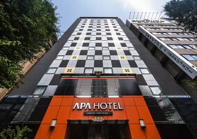 Hotellin julkisivu on koristeltu ruutukuviolla, sen huomiota herättävä pääovi on oranssi, ja kyltissä lukee, että kyseessä on APA HOTEL.