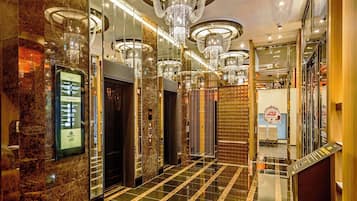 Un moderno vestíbulo de hotel con suelos de mármol, varios ascensores y un candelabro central.