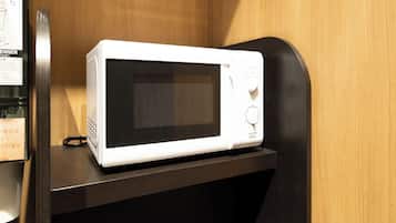 A white microwave on a dark wooden shelf in a room with wooden walls.