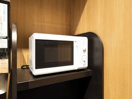 Un four à micro-ondes blanc est posé sur une étagère en bois foncé, dans une pièce aux murs en bois.