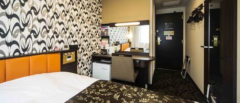 A hotel room with a bed, a desk with a chair, a small kitchenette, a mirror, and a door.