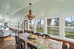 Une pièce spacieuse avec une grande table à manger, de nombreuses chaises et un lustre. La pièce est dotée de grandes fenêtres qui offrent une vue sur l’extérieur.