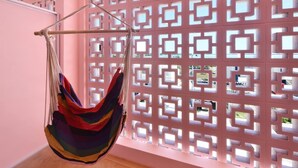 A hammock suspended from a metal rod in a room with a pink wall and a decorative lattice partition.