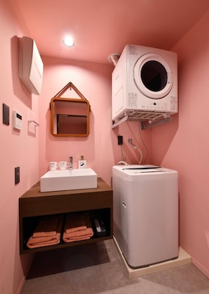 A bathroom with a sink, mirror, towel rack, and a wall-mounted washing machine. - Hotel Pink Hibiscus (Miyakojima)