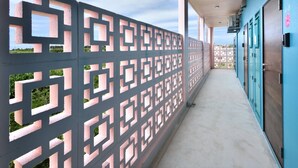 A corridor with a patterned metal fence, a concrete floor, and blue doors on the right.