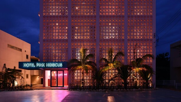 A hotel with a modern facade featuring a grid of square windows and a neon sign for "HOTEL PINK HIBISCUS".