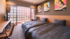 A hotel room with a large bed, a desk, and a chair. There are two wall-mounted artworks depicting a woman.