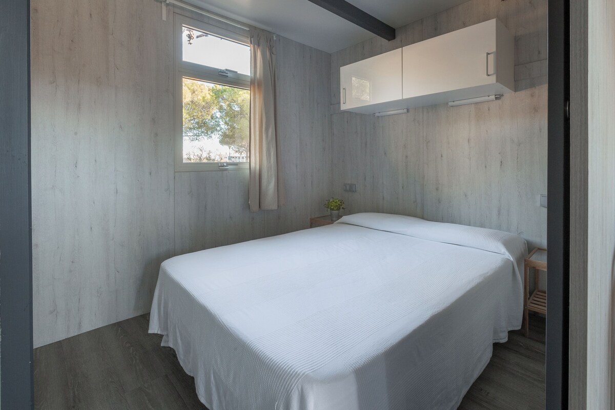 Une chambre à coucher avec un lit, une fenêtre avec des rideaux, un plancher en bois et une armoire blanche.