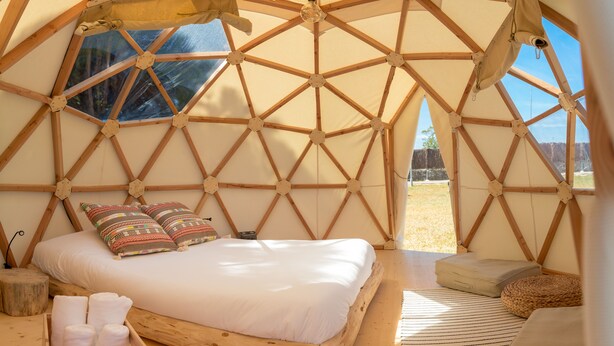 A cozy, wooden-framed tent with a bed, pillows, and a small seating area.