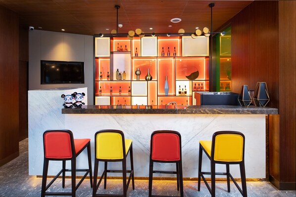 Zona de bar con mostrador de mármol, estantes con botellas y sillas de colores.