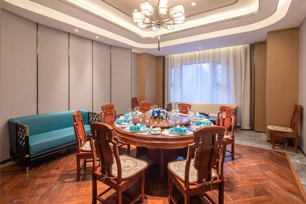 A dining area with a round table set for eight, surrounded by wooden chairs with cushioned seats. A blue sofa is positioned against the wall. - Hampton by Hilton Changchun Ziyou Road (Changchun)