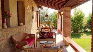 A covered patio area with wicker furniture, a brick wall, and a view of a garden.