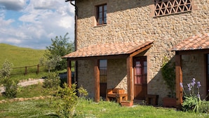 A stone house with a tiled roof, a wooden porch, and a small window.