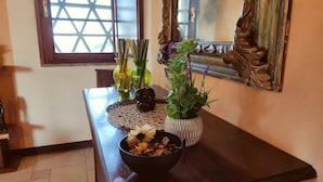 A wooden console table with decorative items including a bowl of dried mushrooms, a potted plant with purple flowers, and two green vases.