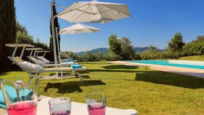 A poolside area with lounge chairs, umbrellas, and a table with glasses of a pink drink.