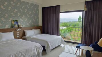 Hotelkamer met twee bedden, een balkon met uitzicht op groen en een zithoek met een tafel en stoelen.
