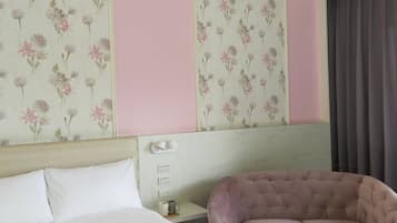 A hotel room with a bed, a pink upholstered chair, and floral wallpaper.