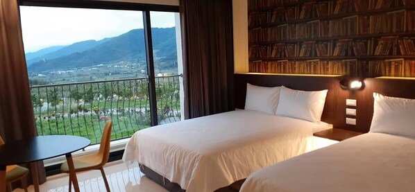 A hotel room with two beds, a bookshelf, a balcony with a view of mountains, and a small table with a chair. - Chulu Manor Hotel (Beinan)