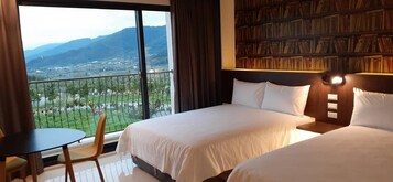 Habitación de hotel con dos camas, una estantería, un balcón con vistas a las montañas y una pequeña mesa con una silla.
