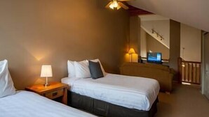 Ett hotellrum med två sängar, ett skrivbord med en lampa, en tv och en trappa som leder upp till en övre våning.