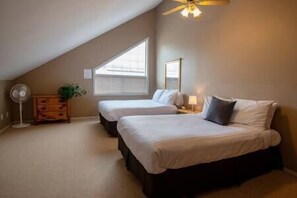 A bedroom with two beds, a ceiling fan, a dresser, and a window with blinds. - 2 BDR with Loft / Mountain Views / Walk Out Deck (Fernie)