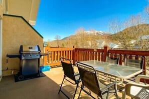 An outdoor patio with a grill, a table, and chairs, overlooking a mountainous landscape. - 2 BDR with Loft / Mountain Views / Walk Out Deck (Fernie)