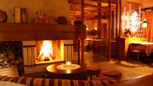 A cozy living room with a fireplace, a round wooden table, and striped cushions. - Hotel Zebru (Stelvio)