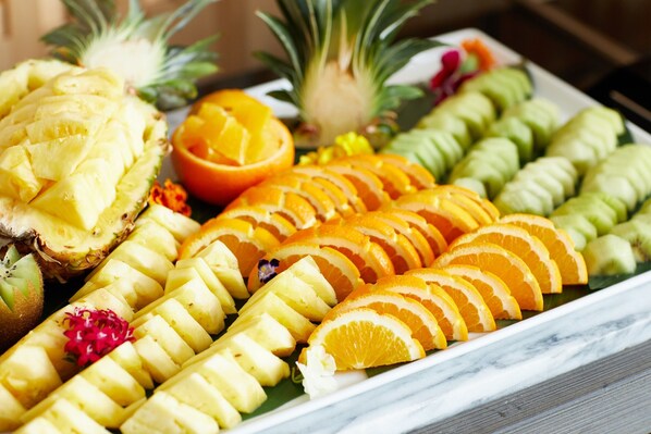 Variedad de frutas cortadas, entre ellas piña, naranja y mango, dispuestas sobre una superficie de mármol.