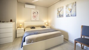 Un dormitorio con cama, lámparas de noche, ventilador de techo, aire acondicionado, una silla y obras de arte en la pared.