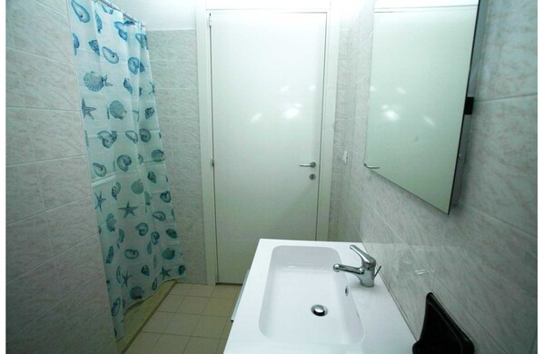 A bathroom with a white sink, a mirror, and a shower curtain with a sea shell pattern. - Appartamenti Boschetto (San Michele al Tagliamento)