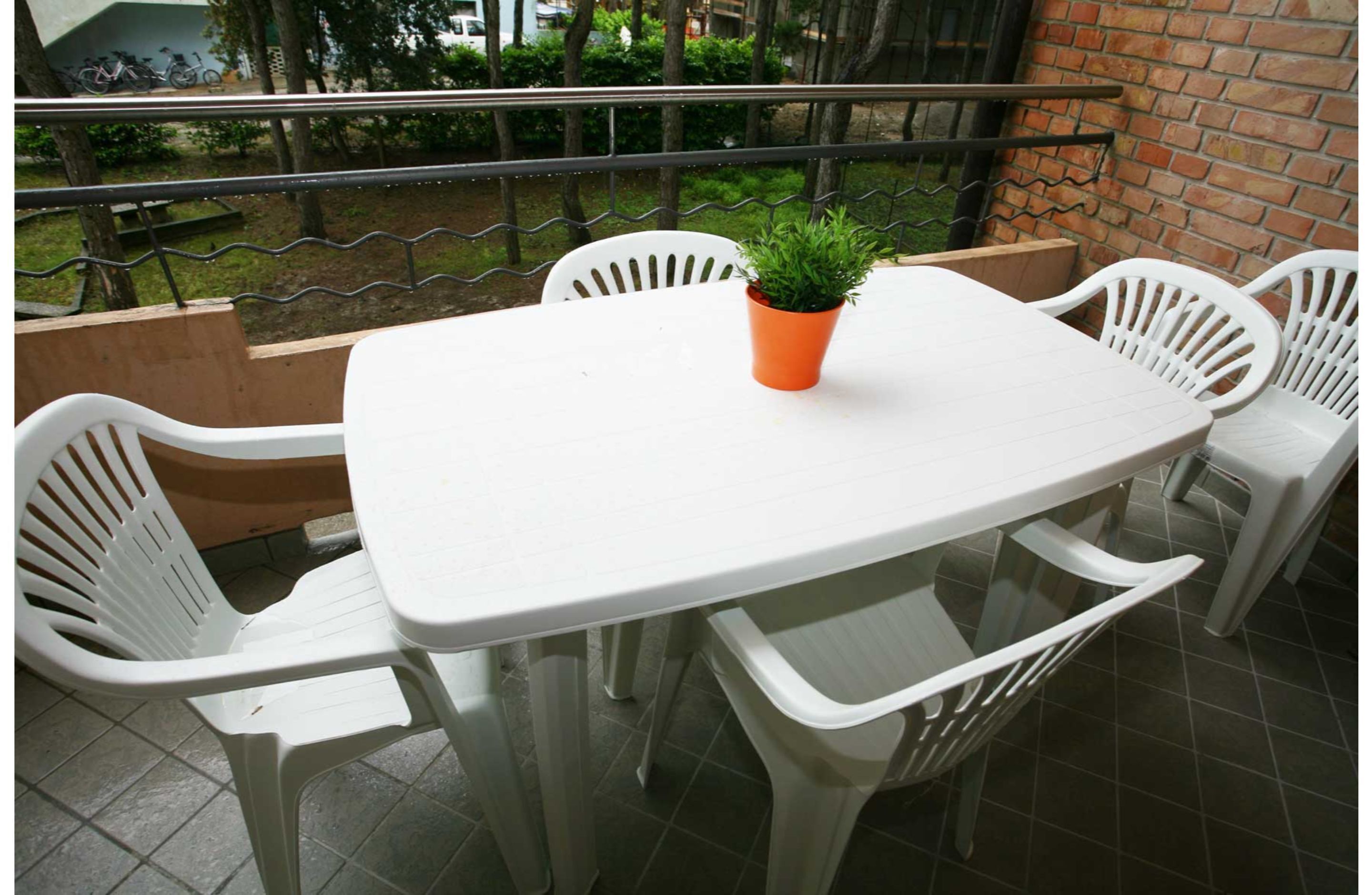 Una mesa blanca de plástico con cuatro sillas, una planta en maceta y un muro de ladrillo al fondo.