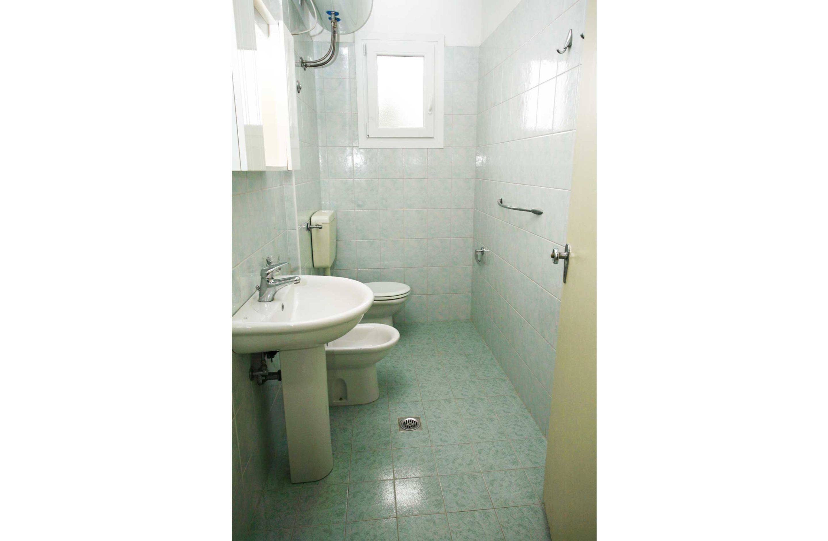 A small, clean bathroom with a sink, two toilets, and a window.