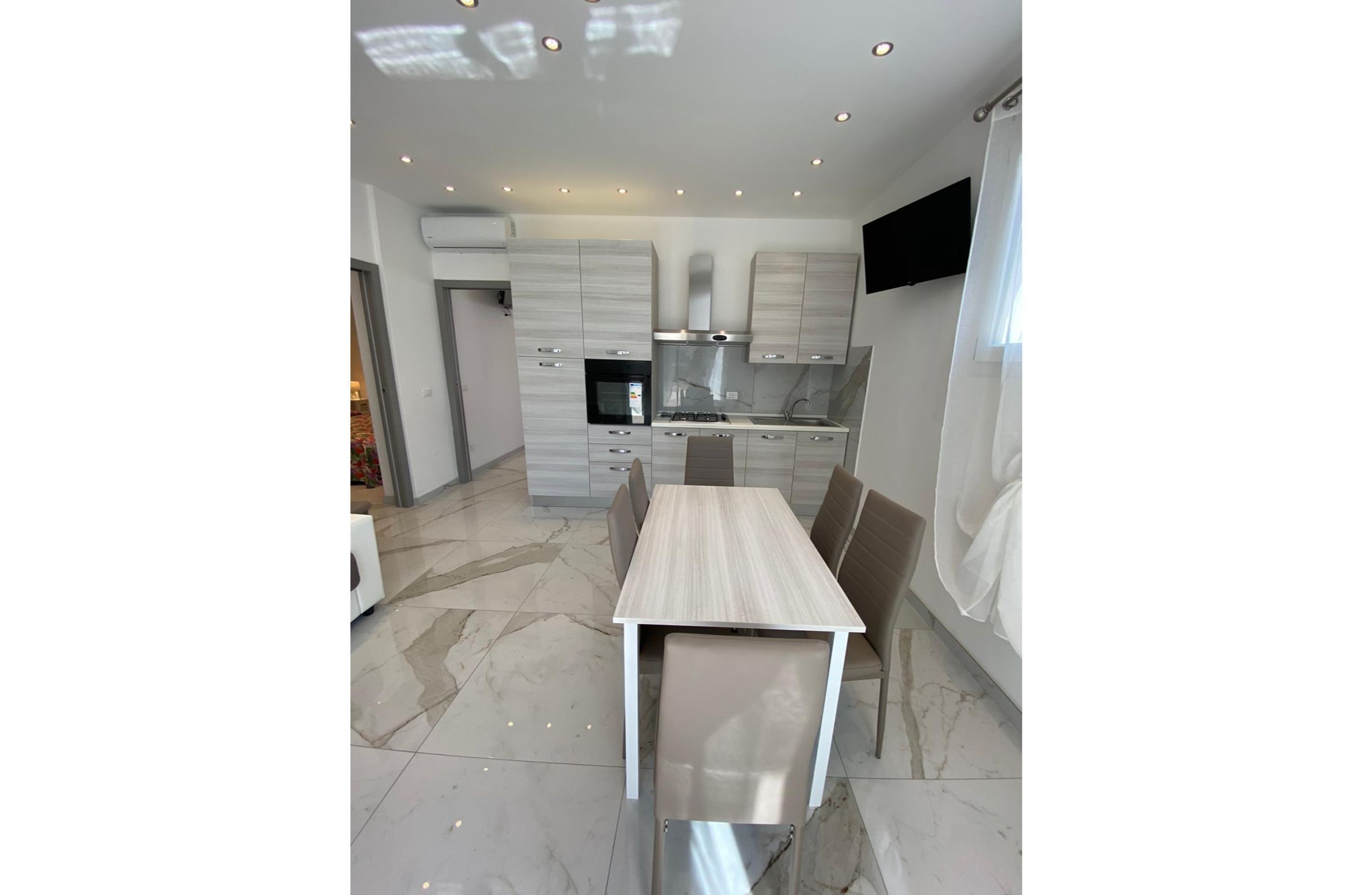 Una cocina moderna con comedor, que presenta piso de mármol, armarios empotrados y un televisor de pantalla plana.