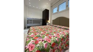 A bedroom with a bunk bed, a large bed with a floral bedspread, a headboard, a window, and recessed ceiling lights. - Appartamenti Boschetto (San Michele al Tagliamento)