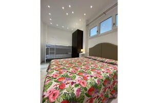Una camera da letto con un letto a castello, un letto grande con copriletto floreale, una testiera, una finestra e faretti a soffitto.