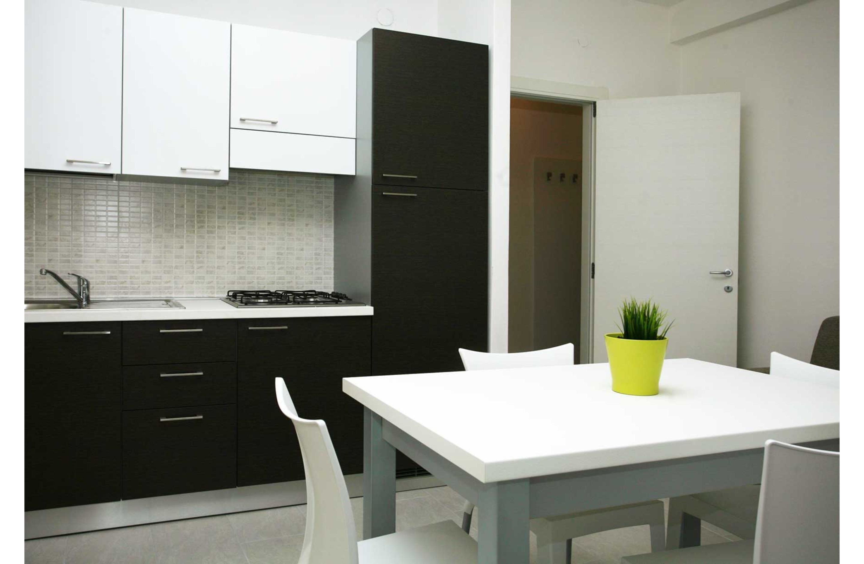 Une cuisine moderne avec des meubles blancs et noirs, un plan de travail blanc et une petite table agrémentée d’une plante jaune.