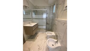 A modern bathroom with a glass-enclosed shower, a sink, a bidet, and marble flooring. - Appartamenti Boschetto (San Michele al Tagliamento)
