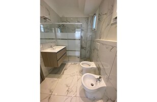 Un bagno moderno con doccia vetro, lavandino, bidet e pavimento in marmo.